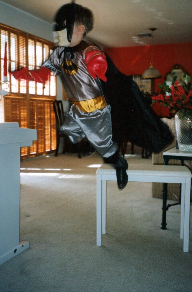 Taylor in a Batman costume, jumping mid-air