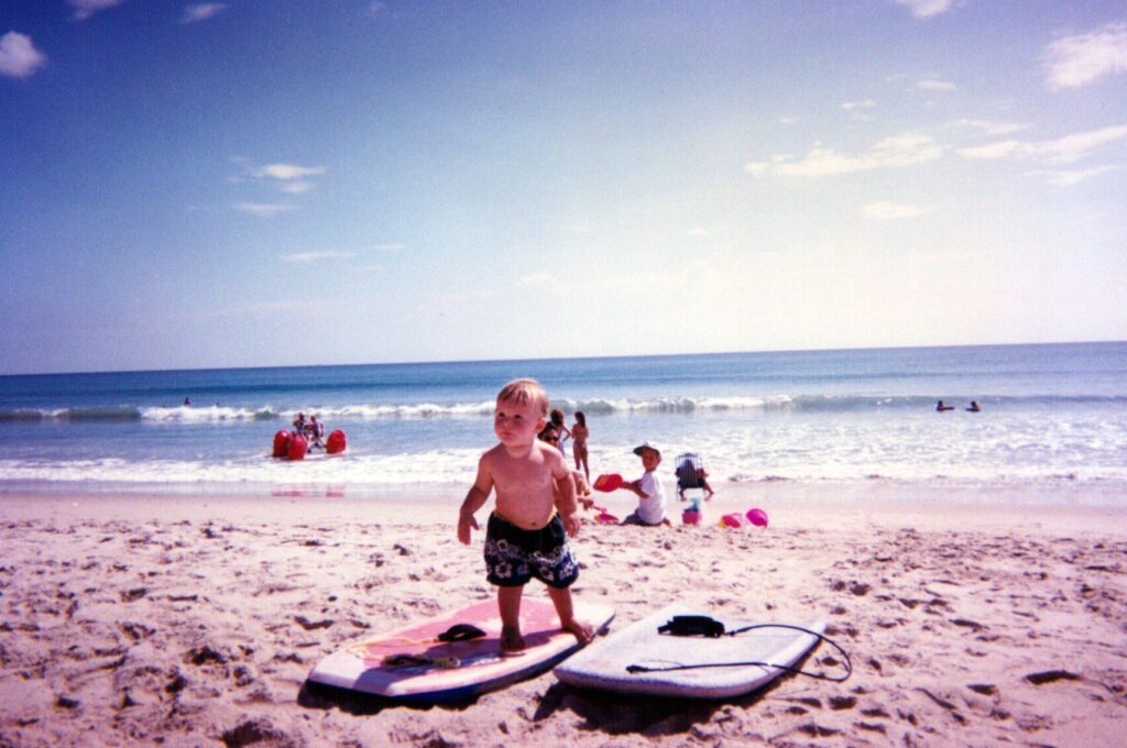 Toddler Taylor on a boogie board in the sand in front of the ocean